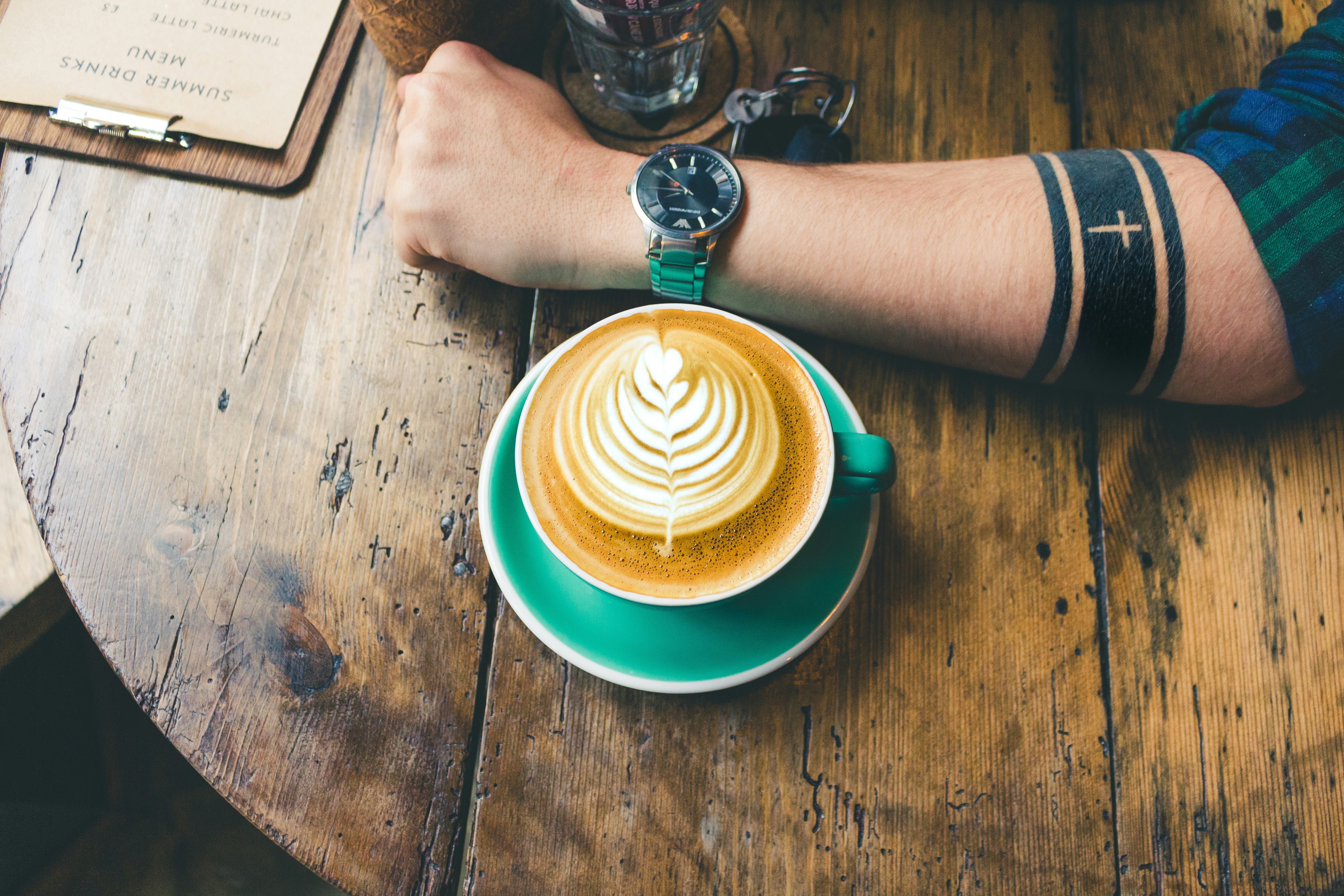 cappuccino next to man's arm whose wearing watch